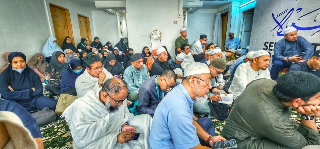 Jemaah haji lelaki dan wanita duduk di atas permaidani mendengar kuliah dalam sebuah bilik di Makkah