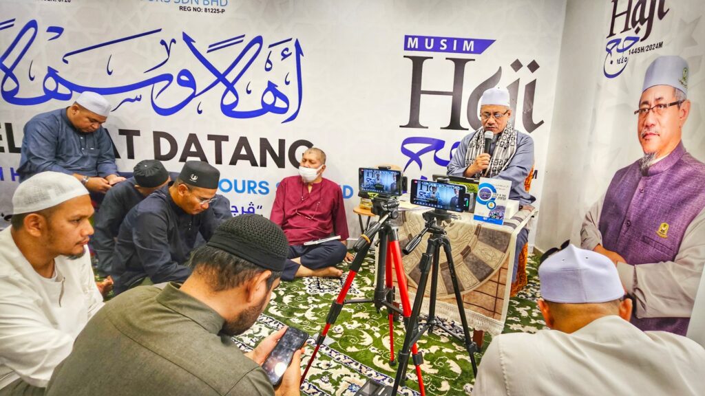 Dr. Abu Anas Madani menyampaikan tazkirah kepada jemaah lelaki yang duduk bersila di hadapan latar Musim Haji 1445H/2024M