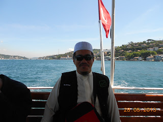 Seorang ahli rombongan berkopiah di atas feri yang menyusuri Selat Bosphorus, dengan bendera Turki di belakang