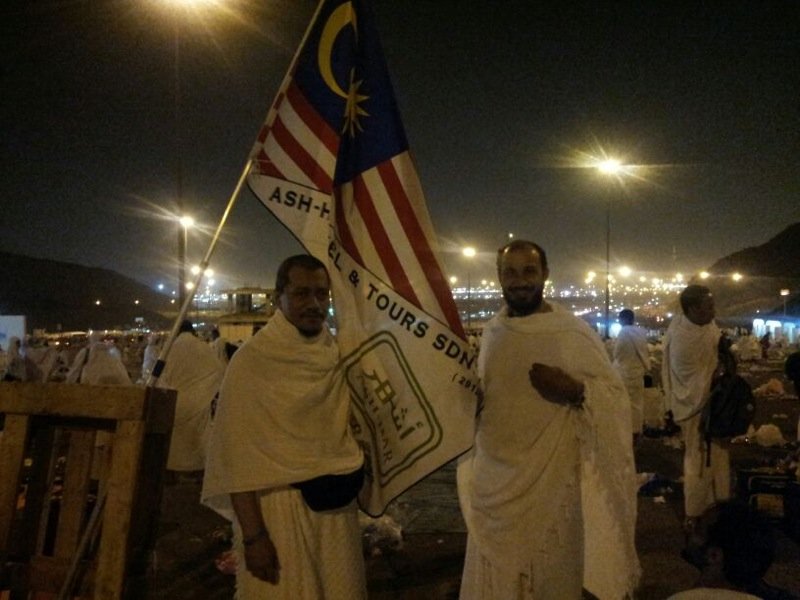 Jemaah berihram memegang bendera Malaysia dan panji Ash-Har Travel pada waktu malam